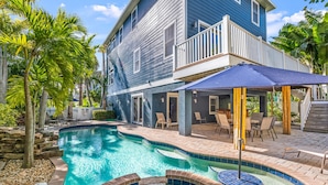 A pool area with a blue house, outdoor furniture, and a small waterfall feature.
