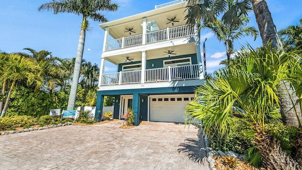 A two-story house with a garage, surrounded by palm trees and greenery.