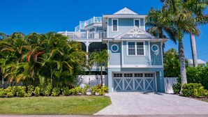 A two-story house with a garage, surrounded by lush greenery and palm trees. - Sunset Views from Rooftop, Heated Pool, Game Room- Caribbean Dream (Holmes Beach)