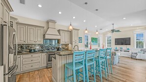 A spacious kitchen with marble countertops, a large island, and blue bar stools. - Sunset Views from Rooftop, Heated Pool, Game Room- Caribbean Dream (Holmes Beach)