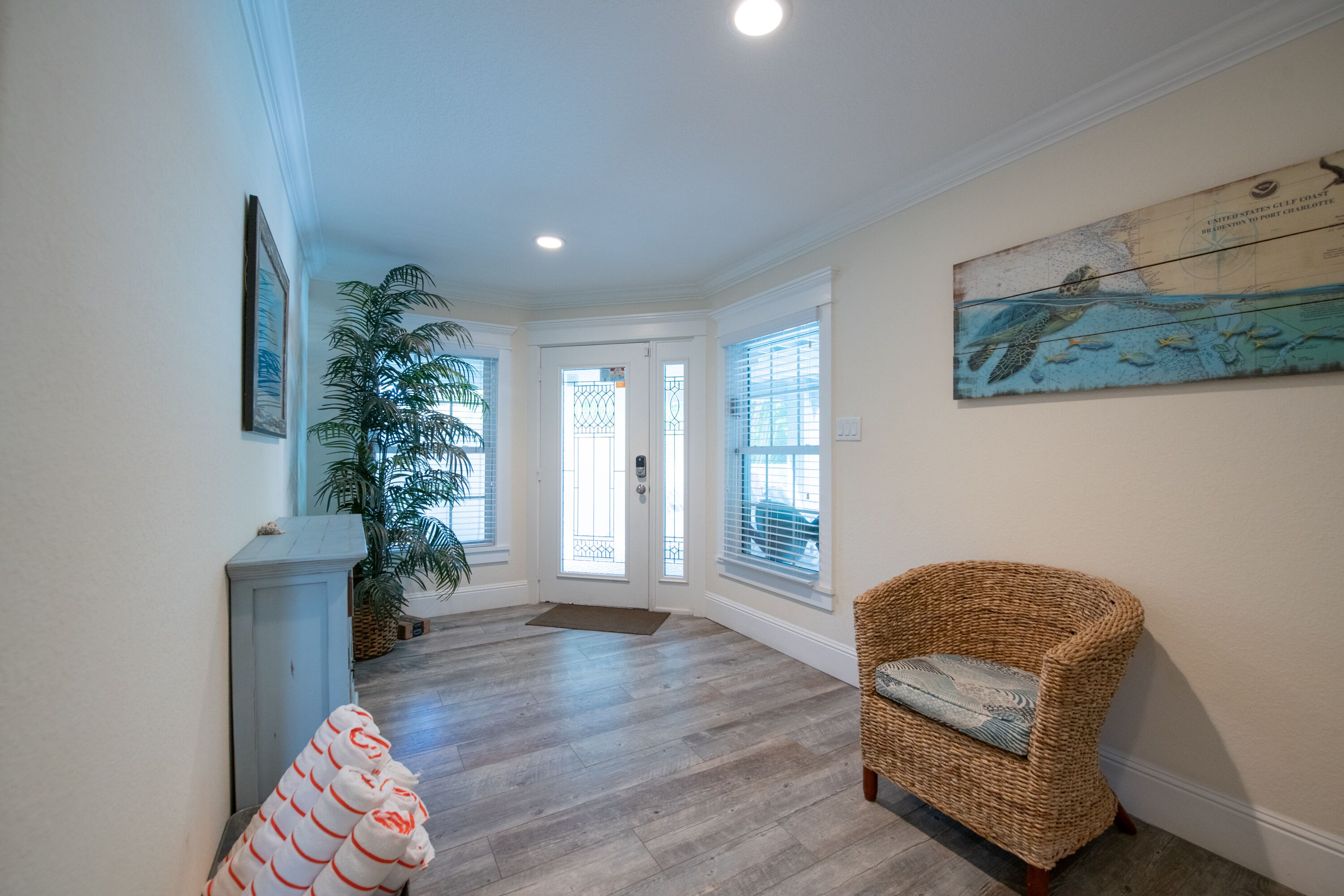 A hallway with a wicker chair, a large potted plant, and a framed map on the wall.