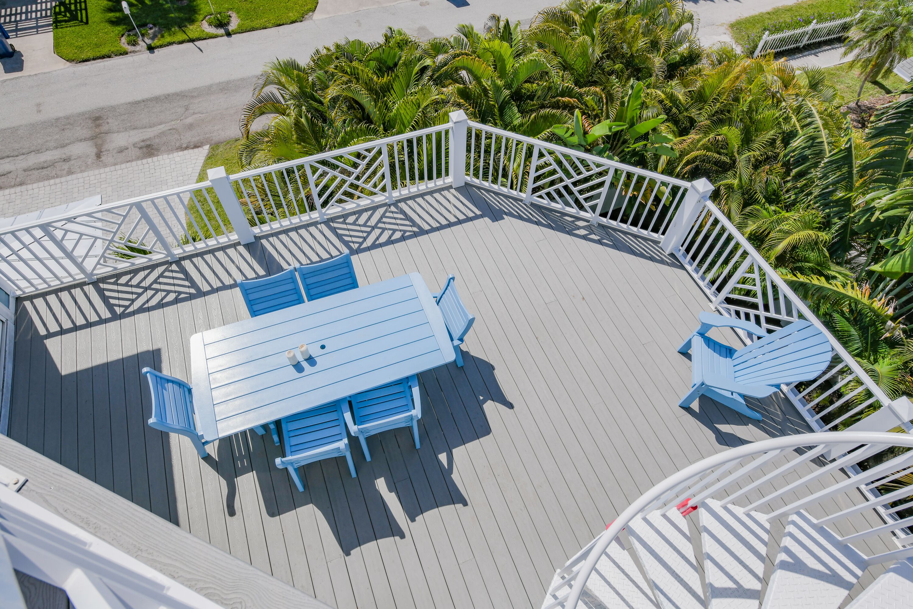 Une terrasse avec une table et des chaises bleues, entourée d’une balustrade blanche, donnant sur un jardin luxuriant.