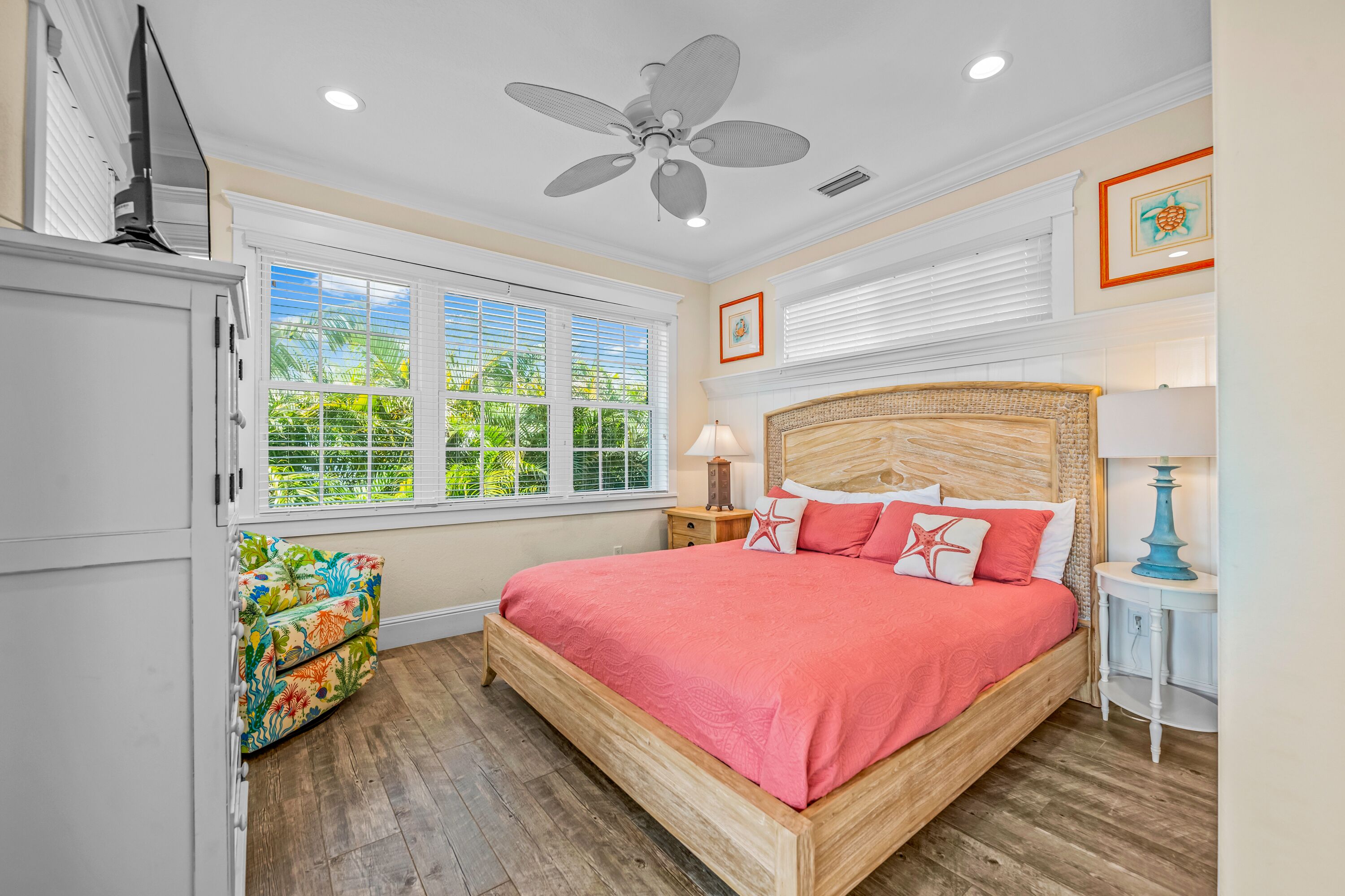 A bedroom with a wooden bed, a ceiling fan, a window with blinds, a nightstand, and a colorful sofa.