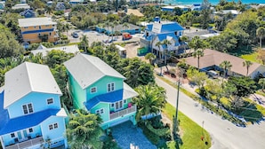 An aerial view of a coastal residential area with houses, palm trees, and a clear view of the ocean.