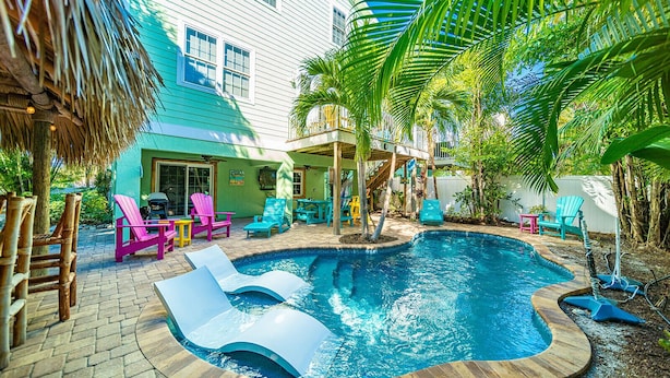 A backyard with a swimming pool, colorful Adirondack chairs, and a covered patio area.