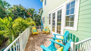 A wooden deck with blue chairs and a small table, surrounded by lush tropical plants.