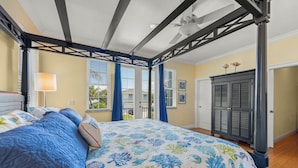 A bedroom with a four-poster bed, a ceiling fan, and a view of the outdoors through large windows.