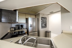 A compact kitchen with stainless steel appliances, a coffee maker, and a chalkboard sign. - Peaceful Escape with Beach Facing Balcony and Pool! (Bradenton Beach)