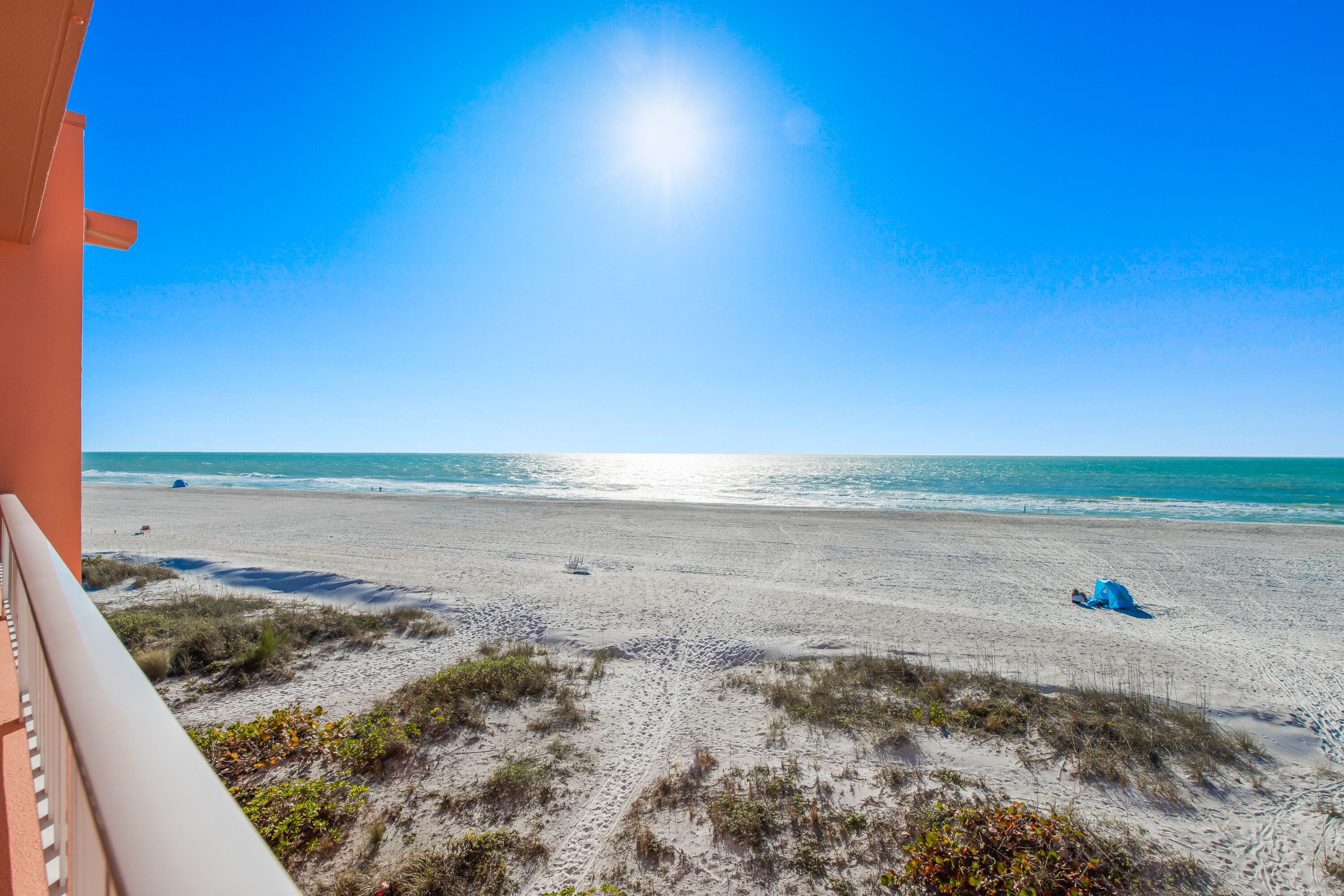 A beach with a clear sky, a person lying on the sand, and a building in the foreground.