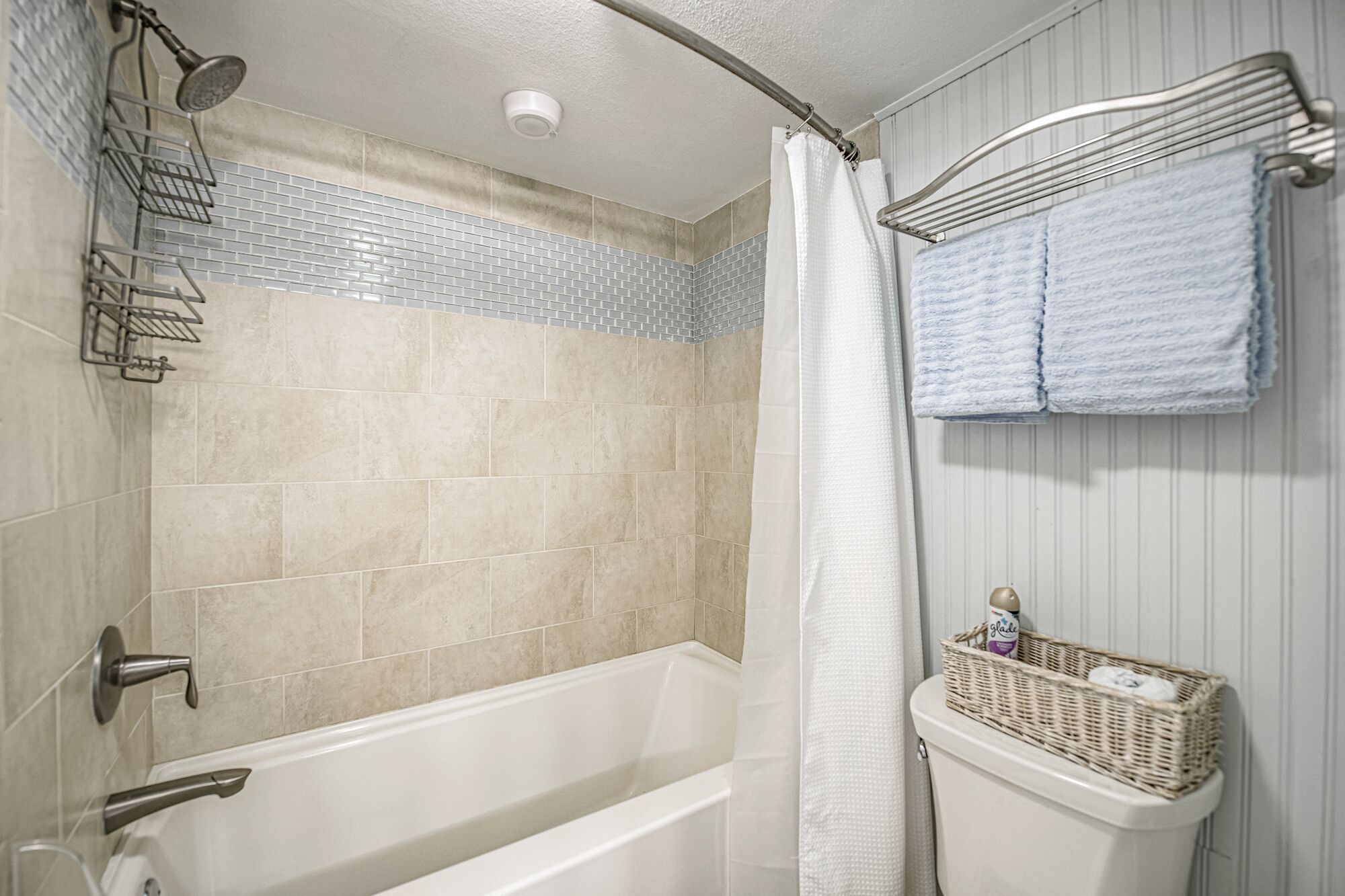 Une salle de bain équipée d’une baignoire, d’une douche et de toilettes. On y trouve un porte-serviettes avec des serviettes et un panier contenant des articles de toilette.