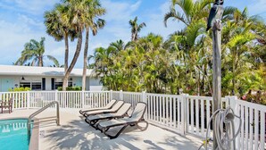 A poolside area with lounge chairs, a white fence, and palm trees. - Cozy Family Duplex with Pool! Close to the Gulf Beaches (Anna Maria)
