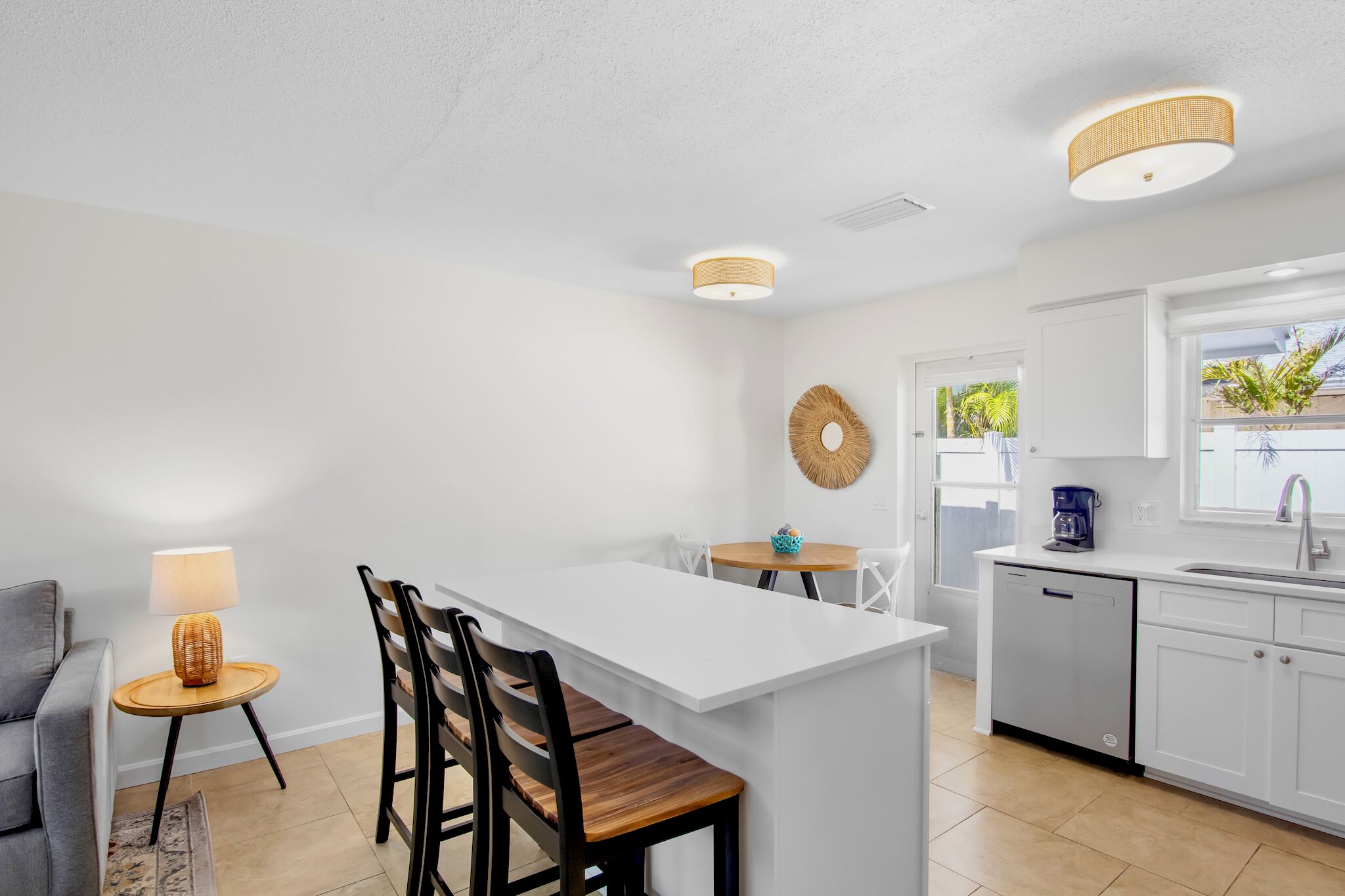A modern kitchen with white cabinetry, a central island, and a dining area with a lamp and chairs.