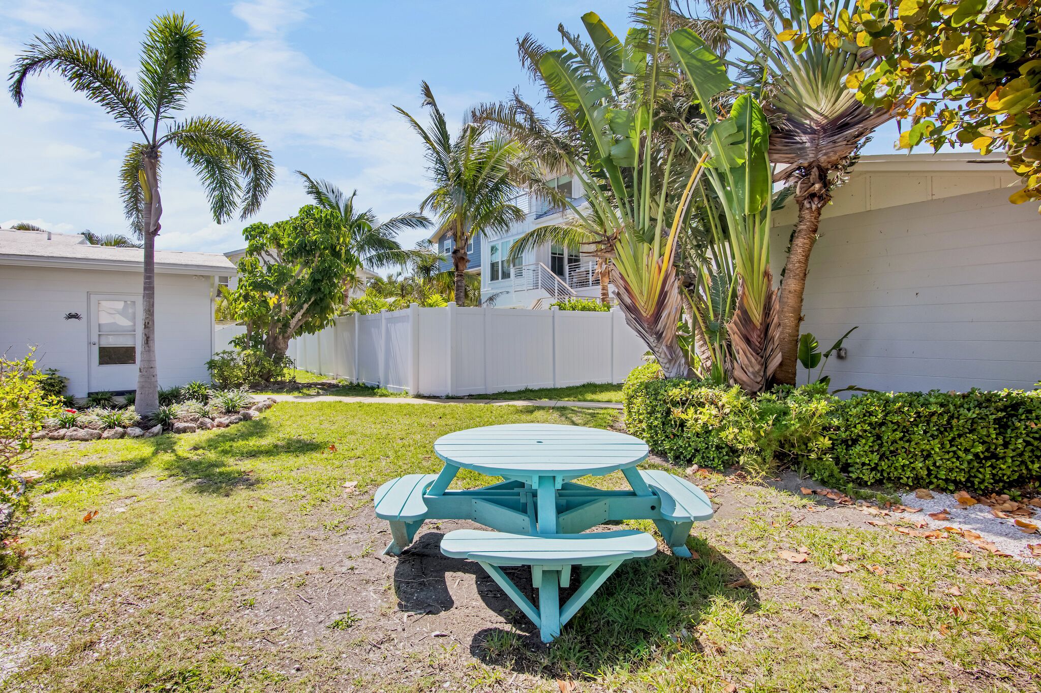A turquoise picnic table in a backyard with palm trees and a white house in the background.