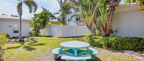 A turquoise picnic table in a backyard with palm trees and a white house in the background.