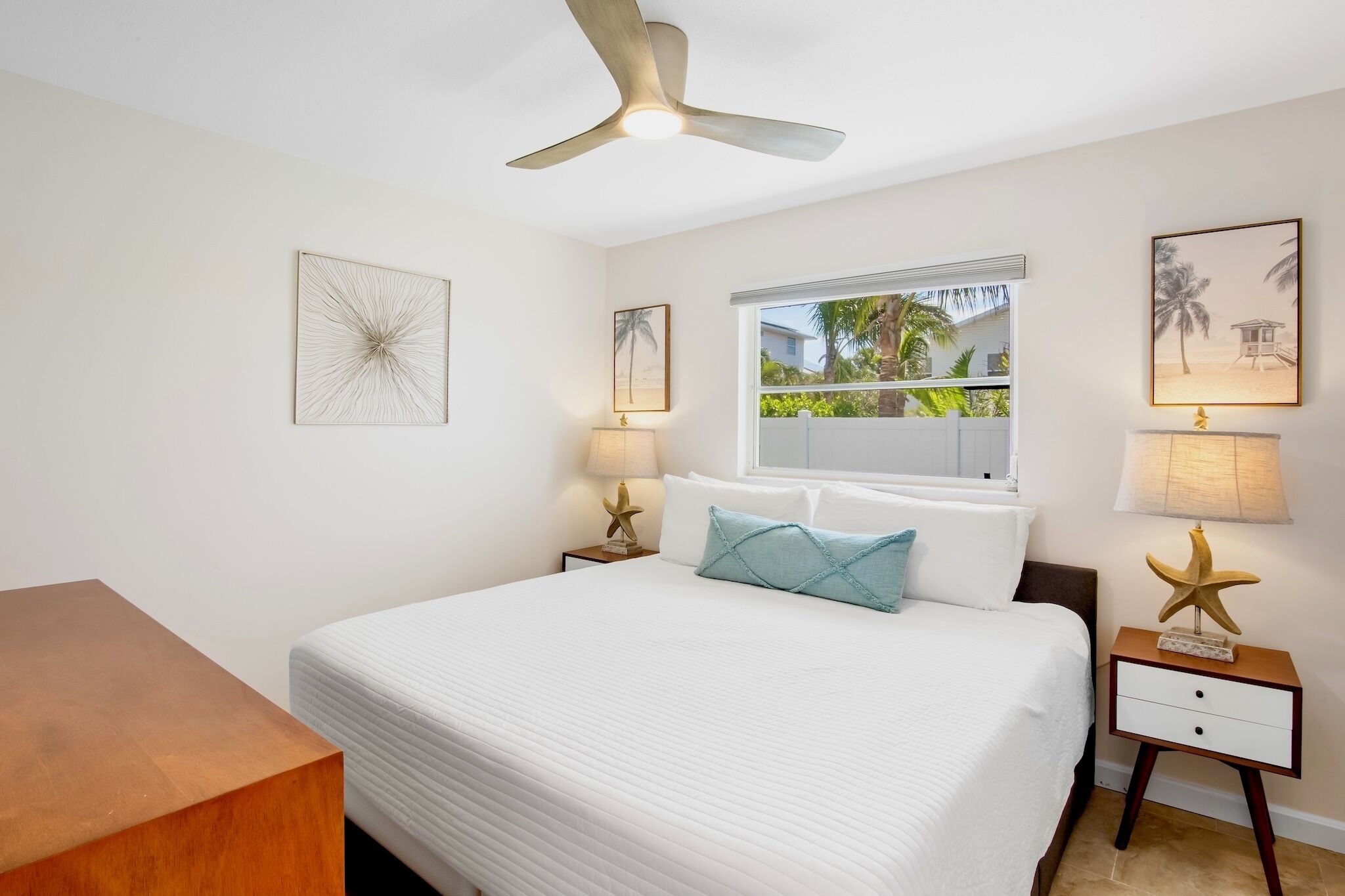 Un dormitorio con cama, ventilador de techo, ventana con vista a follaje y decoración en la pared.