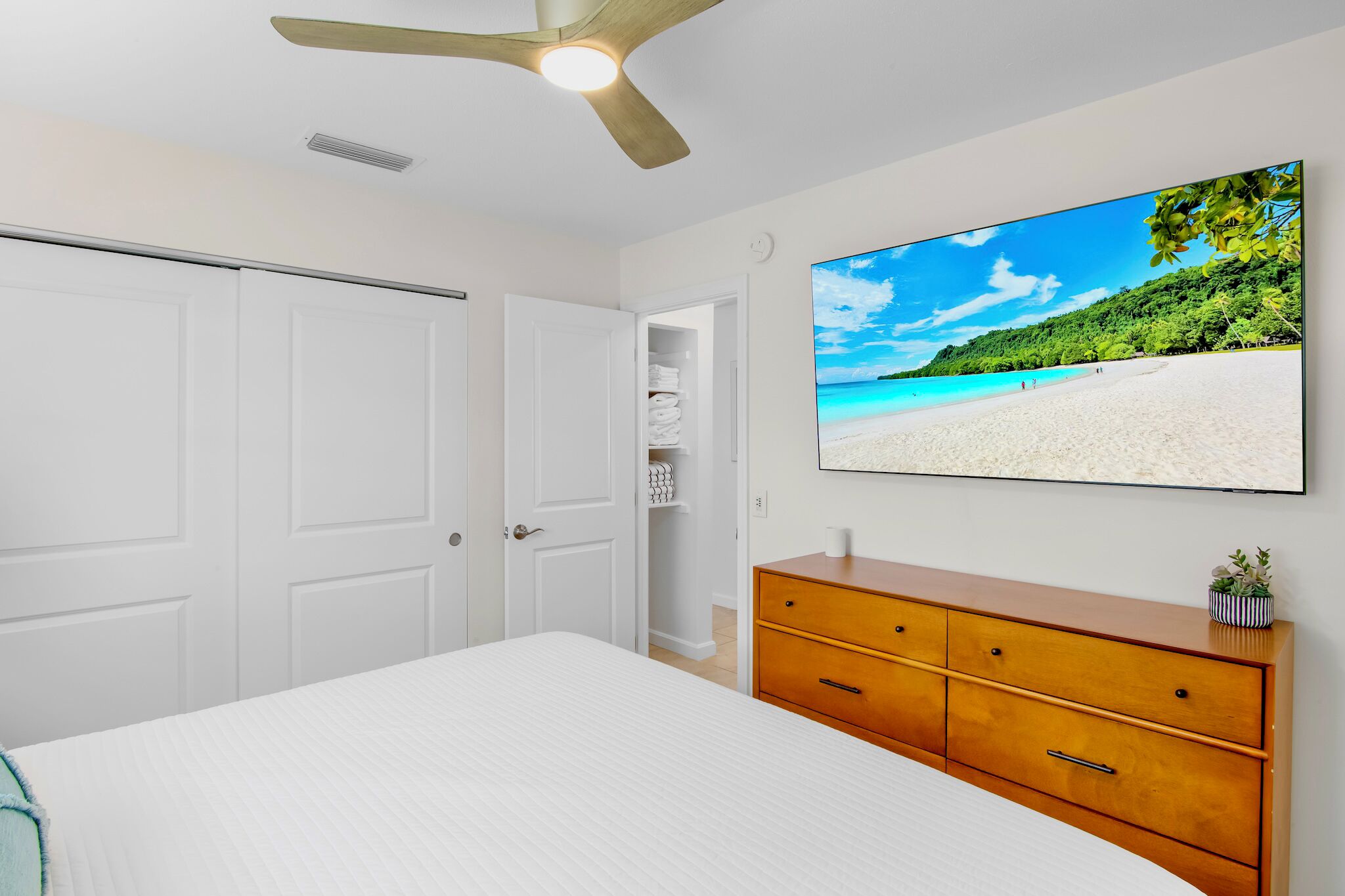 A bedroom with a bed, a wooden dresser, a closet, and a ceiling fan.