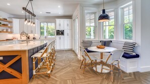 Een moderne keuken met een centraal eiland, barkrukken en een eethoek met een ronde tafel en stoelen.