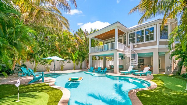 A two-story house with a swimming pool, a covered patio, and a well-maintained lawn.