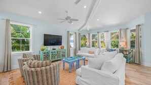 A spacious living room with a white sofa, wicker chairs, a blue coffee table, and a television on a cabinet.