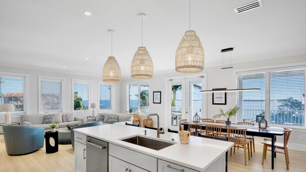 A modern kitchen with a central island, white cabinetry, and a dining area with wooden chairs. - Bayblue — Spacious 6BR Retreat with Pool and Dock! (Bradenton Beach)
