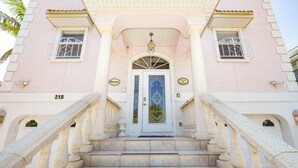 A building with a white facade, a blue door, and a staircase leading to the entrance. - Private Home with Heated Pool, Hot Tub, and Balconies! Near Beach and Dining (Anna Maria)