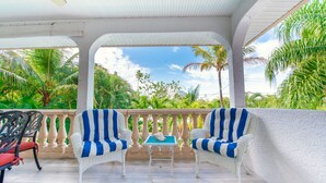 A covered outdoor seating area with two striped chairs and a small table, overlooking lush greenery and a clear sky. - Private Home with Heated Pool, Hot Tub, and Balconies! Near Beach and Dining (Anna Maria)