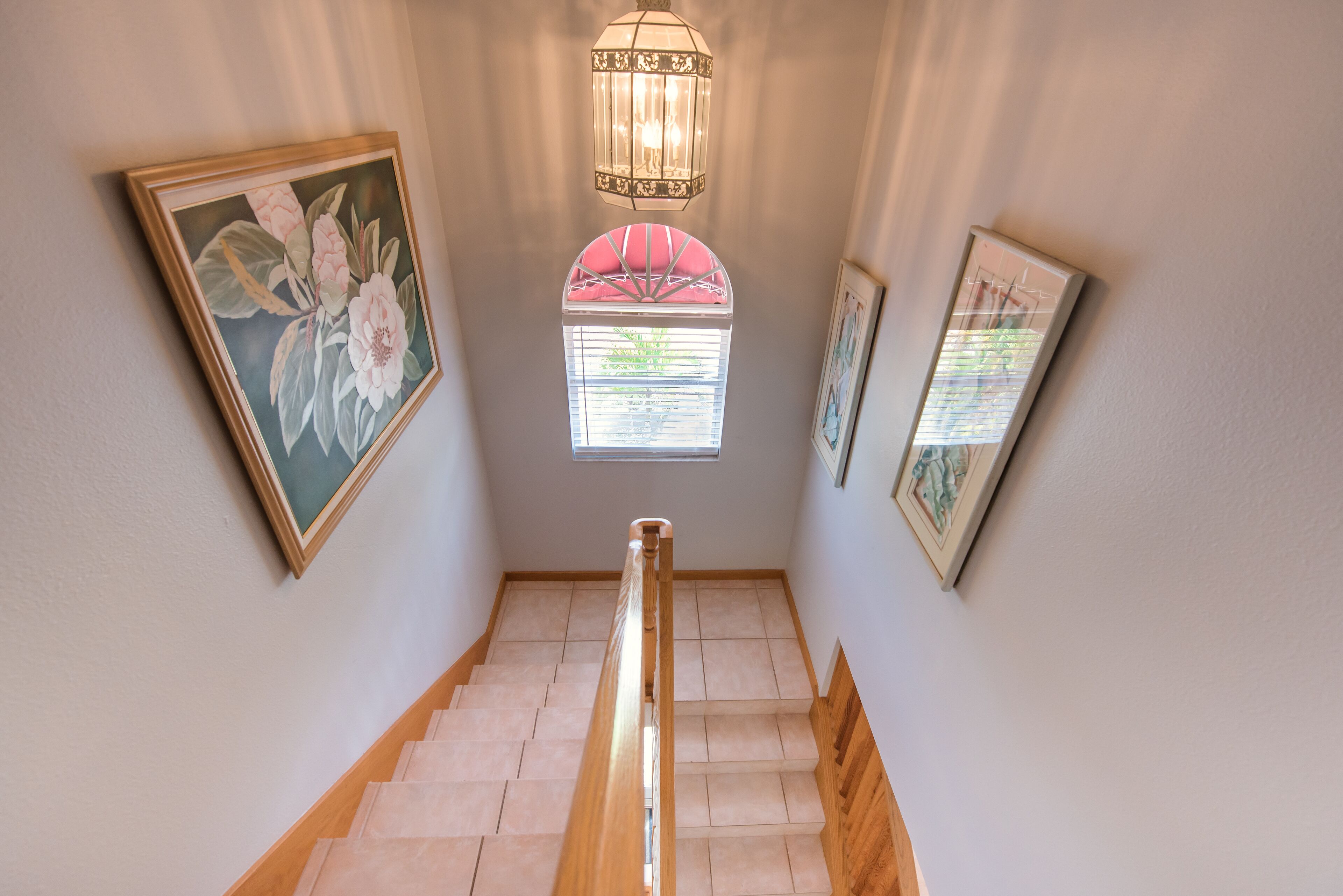 A staircase with wooden handrails, framed artwork on the walls, and a decorative lantern above.