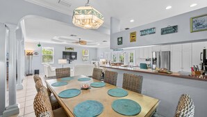 A spacious dining area with a wooden table and woven chairs, a kitchen with white cabinets, and a ceiling fan. - Private Home with Heated Pool, Hot Tub, and Balconies! Near Beach and Dining (Anna Maria)