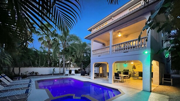 A swimming pool with a two-story building in the background, featuring a balcony with outdoor seating. - Private Home with Heated Pool, Hot Tub, and Balconies! Near Beach and Dining (Anna Maria)