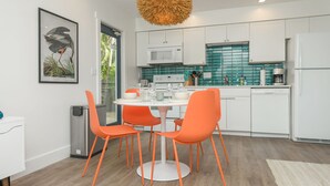 A modern kitchen with white cabinets, a white microwave, and a teal backsplash. There is a dining table with orange chairs and a white floor lamp. - Bungalow with Private Heated Pool! One Block to Beach! - Salty Dog (Holmes Beach)