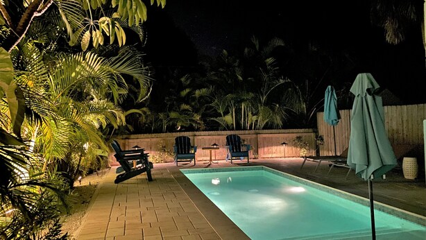 A nighttime swimming pool with a tiled deck, surrounded by palm trees and chairs. - Bungalow with Private Heated Pool! One Block to Beach! - Salty Dog (Holmes Beach)