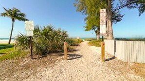 A sandy path leading to a beach with palm trees and a wooden fence. - Bungalow with Private Heated Pool! One Block to Beach! - Salty Dog (Holmes Beach)