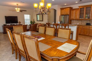 A dining area with a large wooden table, upholstered chairs, a chandelier, and wooden cabinets in the background. - Home with Private Pool, 8 minute walk to Beach! - Villa Portofino (Holmes Beach)