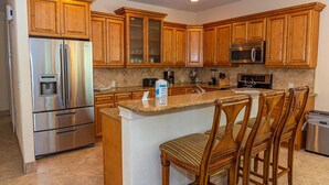 A kitchen with wooden cabinets, stainless steel appliances, a granite countertop, and a bar area with wooden chairs.
