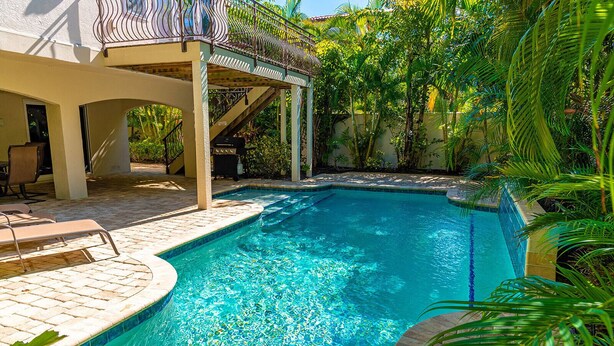 A rectangular swimming pool with clear blue water, surrounded by a tiled deck and lounge chairs.