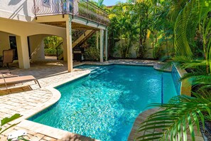 Una piscina rectangular con agua azul cristalina, rodeada por una solana con baldosas y sillas de descanso.