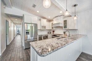 A modern kitchen with white cabinetry, a large island with a marble countertop, stainless steel appliances, and pendant lighting. - Private Home with Pool, Outdoor Dining and Grill! Close to Beach and Pine Ave! (Anna Maria)