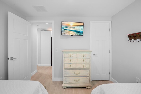 A bedroom with two beds, a dresser, and a TV on the wall.