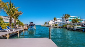 A waterfront property with a dock, lounge chairs, and a boat. - Canal front home with Incredible Rooftop Views and Pool with Spa - Aqua Bay (Holmes Beach)