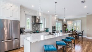 A spacious kitchen with a large island, stainless steel appliances, and a dining area with wooden chairs. - Canal front home with Incredible Rooftop Views and Pool with Spa - Aqua Bay (Holmes Beach)