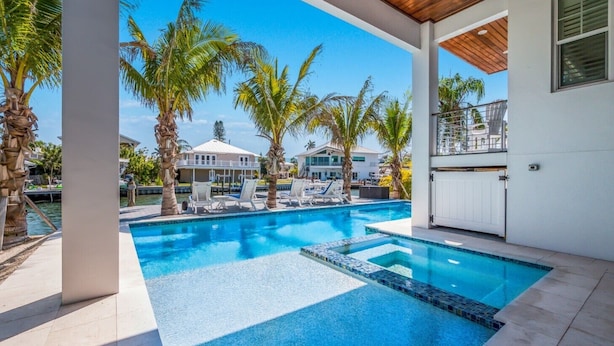A swimming pool with lounge chairs, palm trees, and a view of other buildings. - Canal front home with Incredible Rooftop Views and Pool with Spa - Aqua Bay (Holmes Beach)