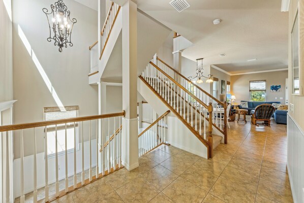 A spacious living area with a wooden staircase, a chandelier, and a blue sofa.