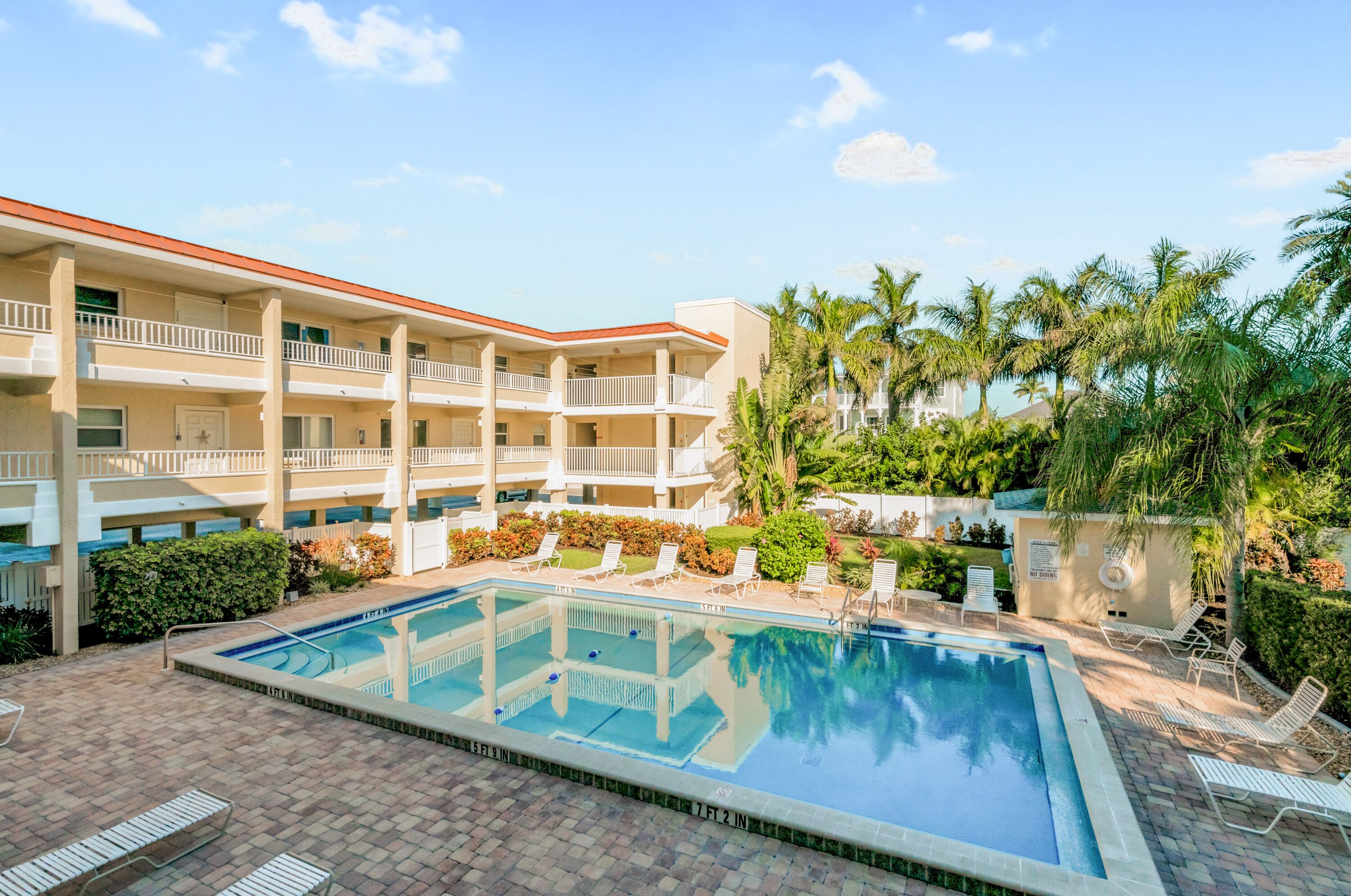 A hotel with a swimming pool, multiple balconies, and palm trees.