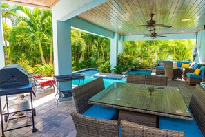 Relax and dine in style on the patio, surrounded by lush greenery and featuring a pool, comfortable furniture, and a dining table.