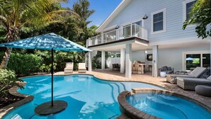 A pool area with two separate pools, a covered patio with outdoor furniture, and a two-story house with a balcony. - Large Private Duplex, Heated Pool and Spa! (Holmes Beach)