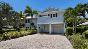 A two-story residential building with a garage, surrounded by well-maintained landscaping and palm trees. - Large Private Duplex, Heated Pool and Spa! (Holmes Beach)