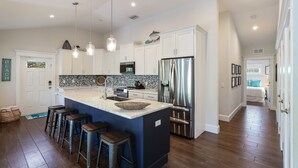 A modern kitchen with white cabinets, a large island with stools, stainless steel appliances, and a backsplash with a black and white pattern. - Large Private Duplex, Heated Pool and Spa! (Holmes Beach)