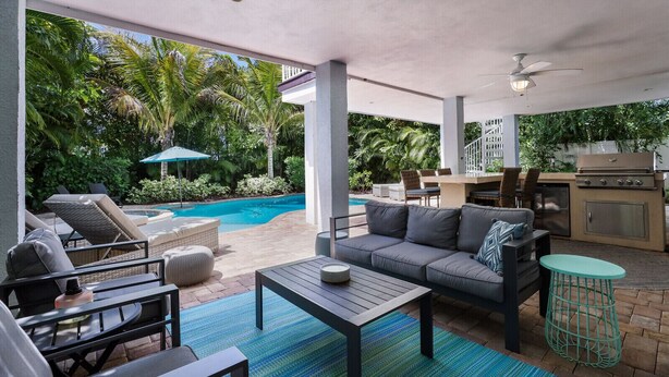 A covered outdoor area with a pool, lounge chairs, a sofa, a table, and a grill. - Large Private Duplex, Heated Pool and Spa! (Holmes Beach)