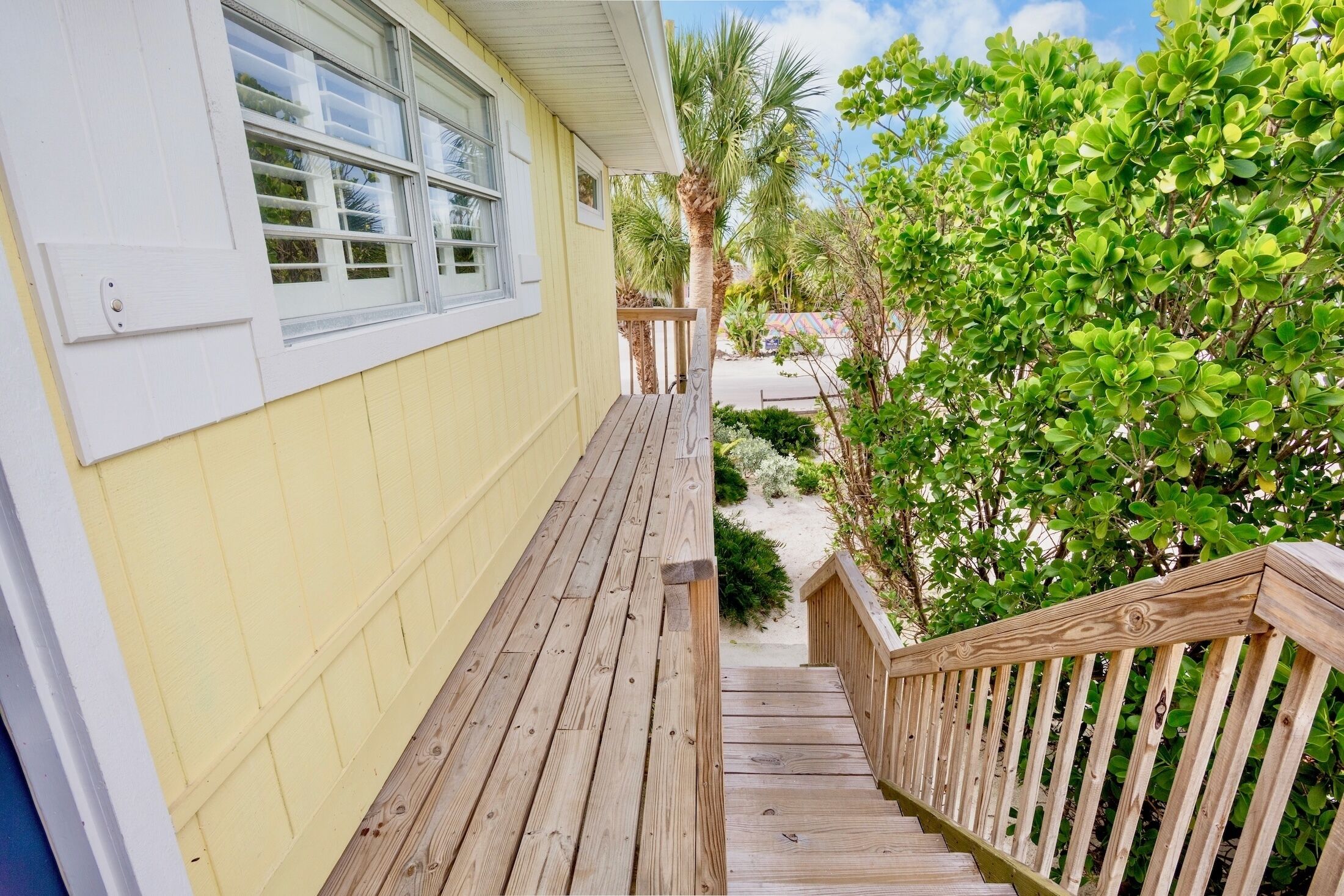 Une terrasse en bois menant à une maison à l’extérieur jaune et aux bordures blanches.