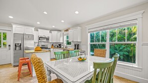 A modern kitchen with white cabinets, stainless steel appliances, and a dining area with a glass table and green chairs.